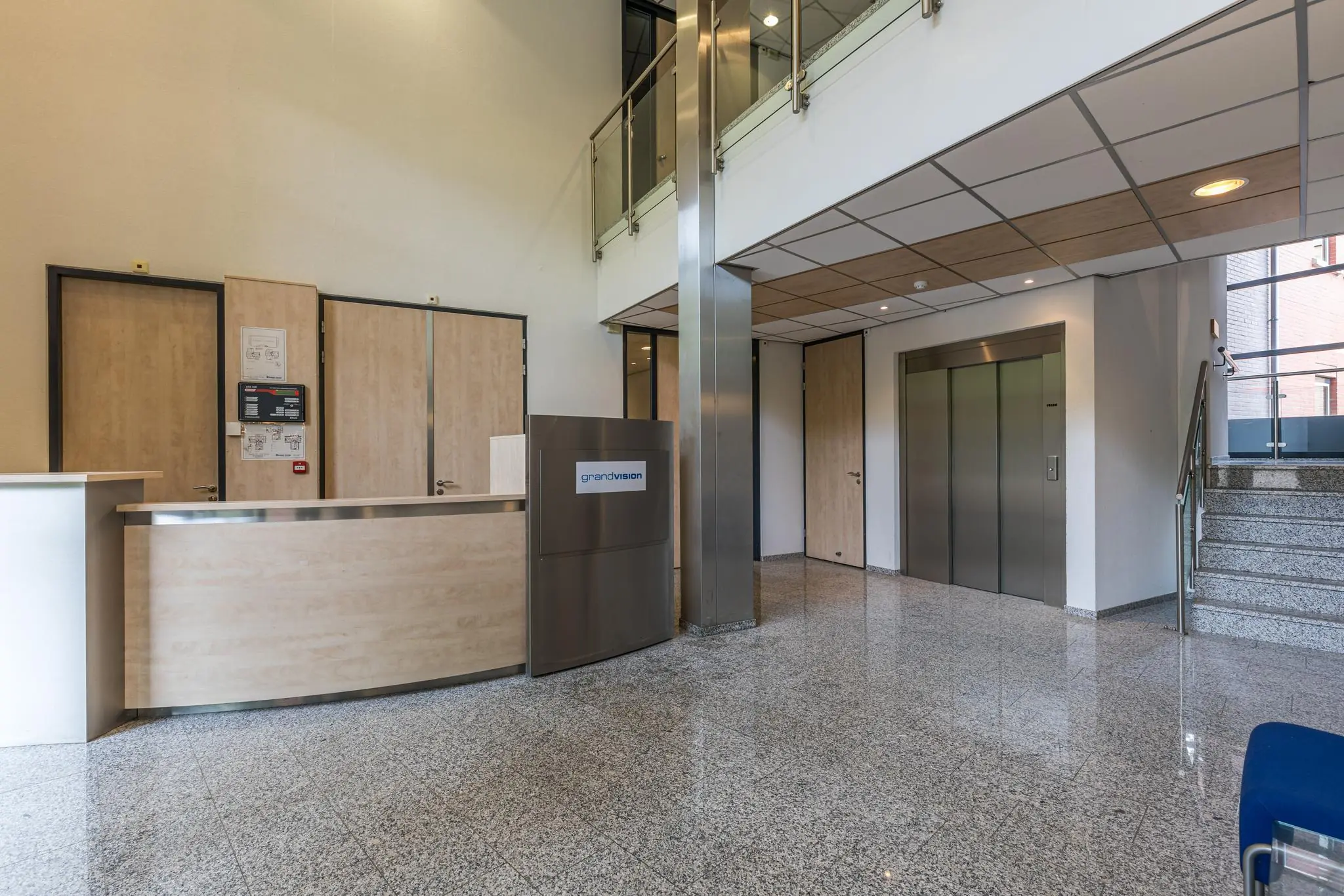 Moderne ontvangsthal met balie, lift, trap en het logo van GrandVision aan de Laan Blusse van Oud Alblas.